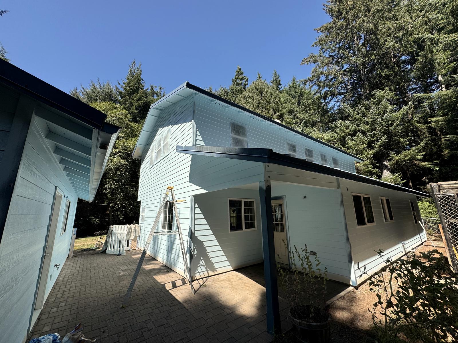The pale blue wing and the garage finished, a step ladder standing on the brick patio between them.