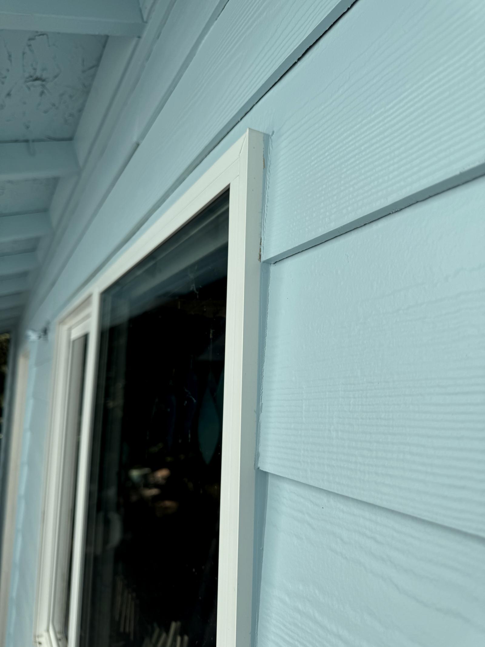 Close on a door frame, the white trim cut clean against pale blue lap siding under the eave.