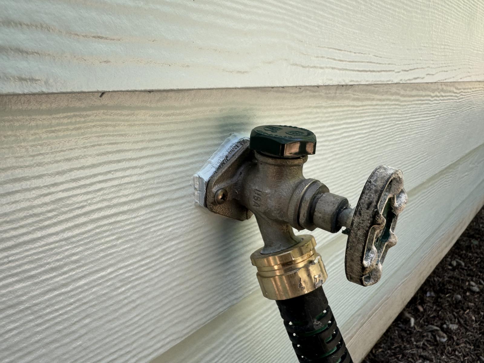A brass hose bib on a freshly painted wall, the siding cut in by hand right up to the fitting.