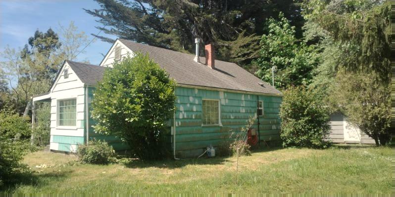 A cottage with teal shingle siding, the paint flaking away to bare wood across the whole wall.