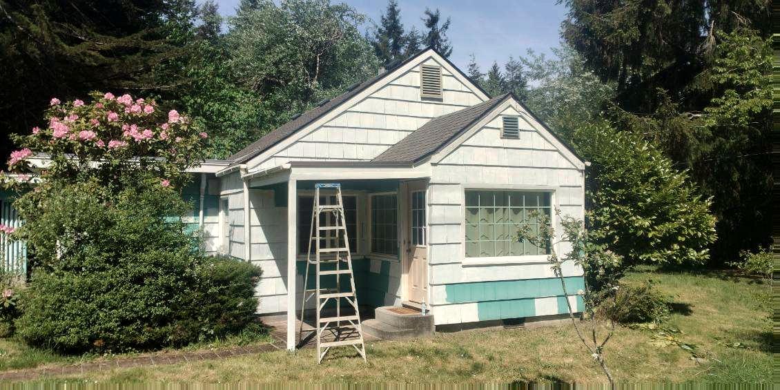 The front of the cottage primed in patches, a step ladder under the porch, ready for the finish coats.