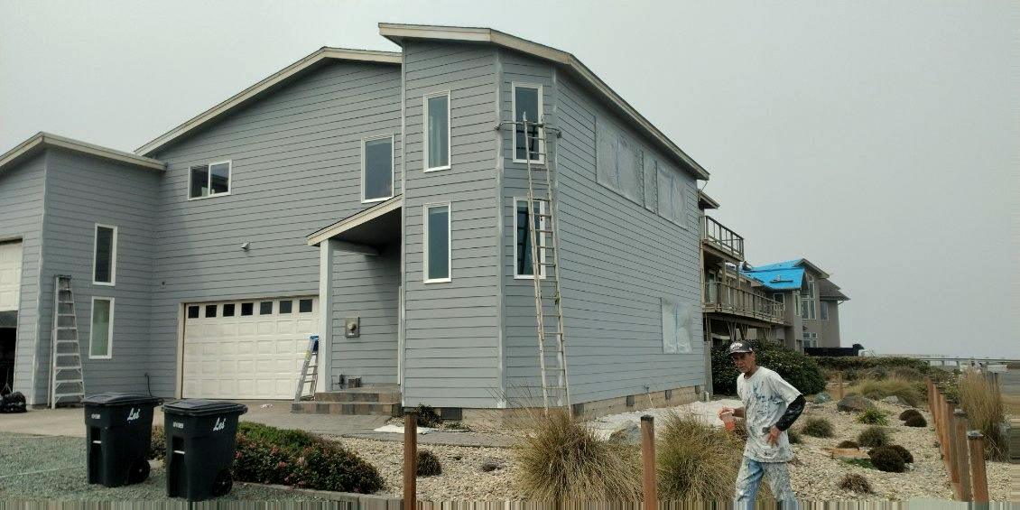 The finished house in gray-blue with white window trim, ladders still standing against the wall.