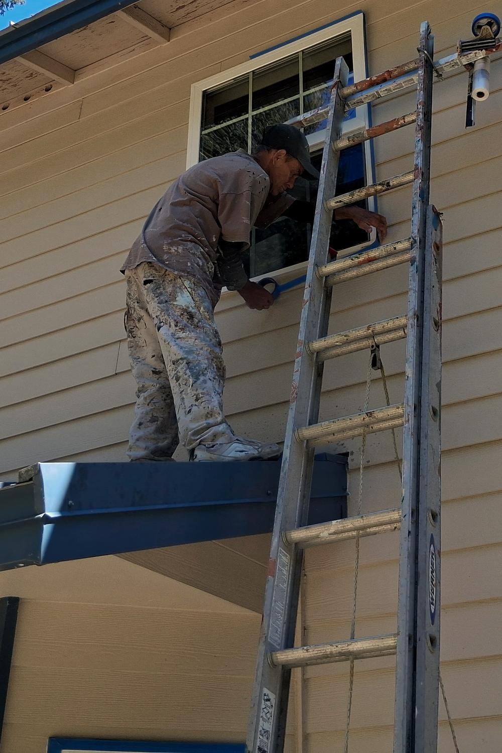 An England Brothers painter on a ladder, cutting in the trim around an upstairs window by hand.